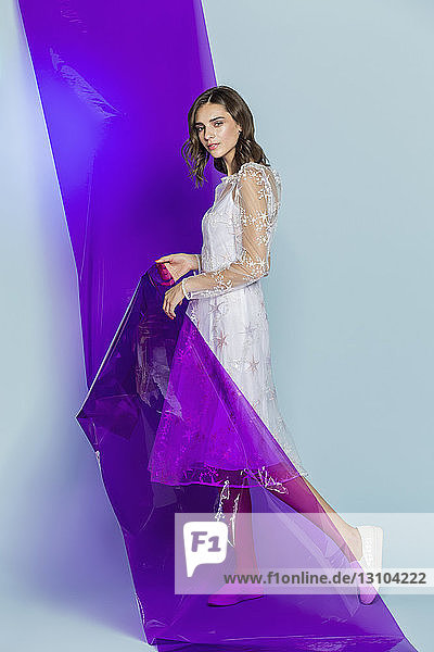 Portrait of a female fashion model posing with purple plastic sheet against blue background