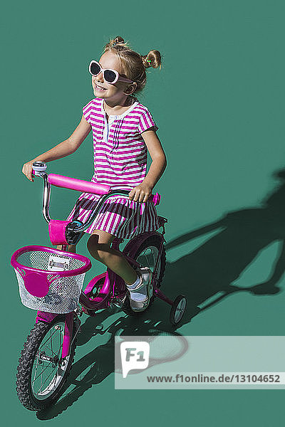 Unbekümmertes Mädchen fährt Fahrrad auf grünem Hintergrund