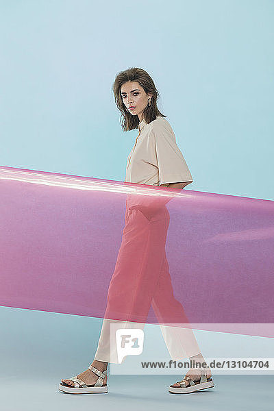 Portrait of a female fashion model posing with pink plastic sheet against blue background