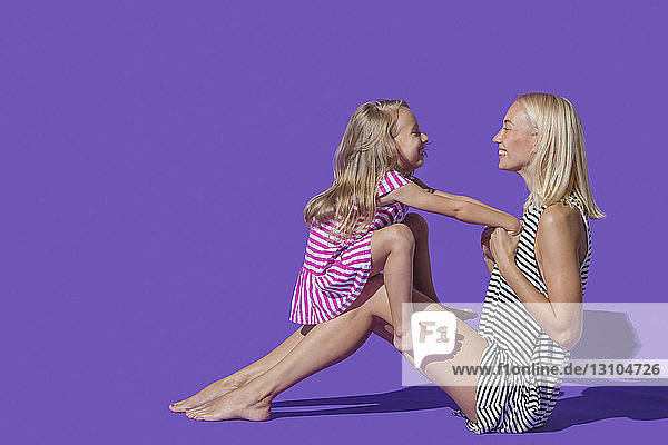 Liebevolle Mutter und Tochter in gestreiften Kleidern vor lila Hintergrund