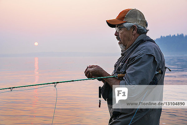 Kaukasischer Mann bindet eine Fliege an seiner Fliegenfischerschnur  während er Lachs und Searun Cutthroat Forelle fischt