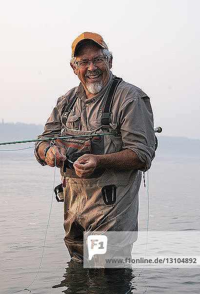 Kaukasischer älterer Mann bindet eine Fliege an seiner Fliegenfischerschnur  während er auf Lachs und Searun Cutthroat Forelle fischt