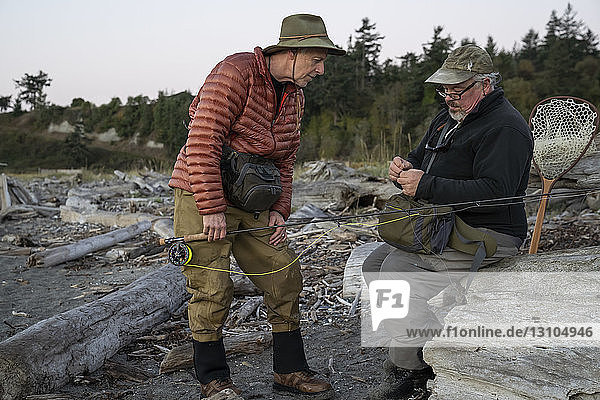 A male fly fisherman watches his guide work putting on a new fly to try for salmon or trout at a salt water beach.