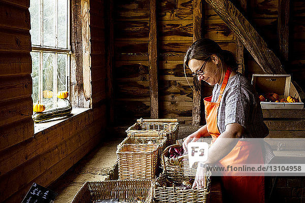 Frau mit Schürze steht im Hofladen und arrangiert Körbe mit Gemüse.