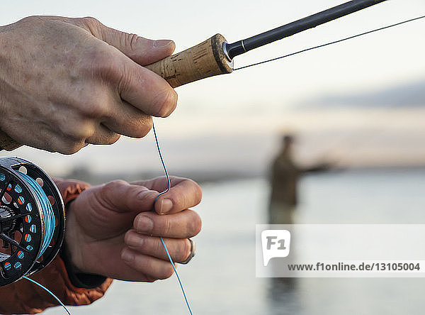 Nahaufnahme der Hände eines Fliegenfischers  der beim Angeln seine Fliegenrute und Schnur hält.