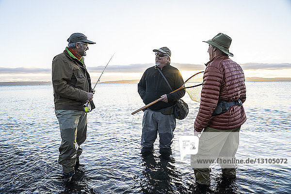 Two fly fisherman talk with their guide about new techniques while fly fishing for searun coastal cutthroat trout at a beach on the north west coastline of the USA.