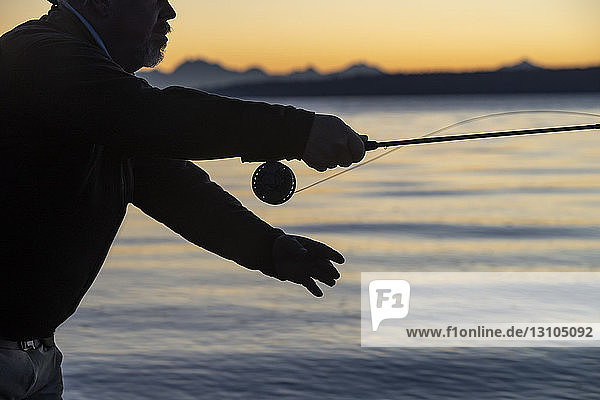 Die Silhouette eines Fliegenfischers  der bei Sonnenaufgang an einem Strand an der Westküste der USA nach Cutthroat-Forellen wirft