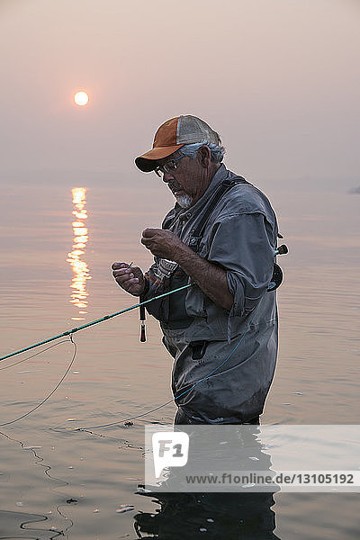 Mann bindet eine Fliege an seiner Fliegenfischerschnur  während er auf Lachs und Seesaibling fischt