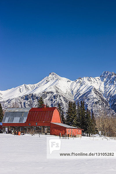 A red roofed barn in a snow-covered field with the Chugach Mountains in the background  South-central Alaska; Palmer  Alaska  United States of America