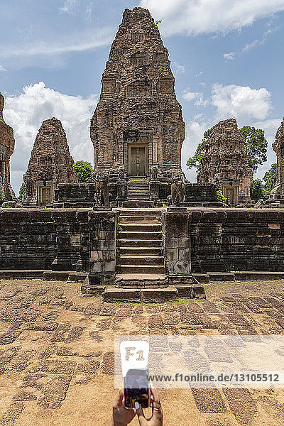 Woman with mobile photographing ruined stone temple  East Mebon  Angkor Wat; Siem Reap  Siem Reap Province  Cambodia