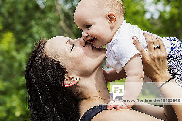Eine junge Mutter verbringt im Sommer viel Zeit mit ihrer Tochter in einem Park und hält sie in die Luft  während sie ihr einen Kuss auf die Wange gibt; Edmonton  Alberta  Kanada