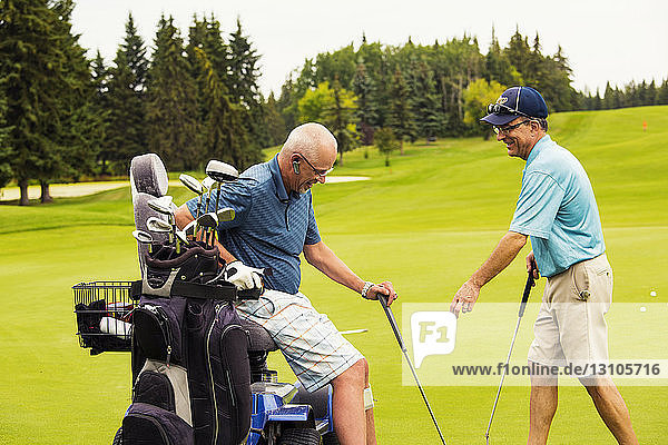 Ein nichtbehinderter Golfer unterstützt einen behinderten Golfer  der einen speziellen elektrischen Golfrollstuhl benutzt  während sie zusammen auf einem Golfplatz den besten Ball spielen; Edmonton  Alberta  Kanada