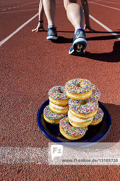 A plate full of candy covered donuts on a running track with a female runner in a lane in a starter stance; Calgary  Alberta  Canada