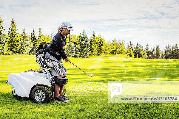 Ein körperlich behinderter Golfer  der einen Ball auf einem Golfplatz schlägt und einen speziellen motorisierten Hydraulikrollstuhl zur Golfunterstützung benutzt; Edmonton  Alberta  Kanada