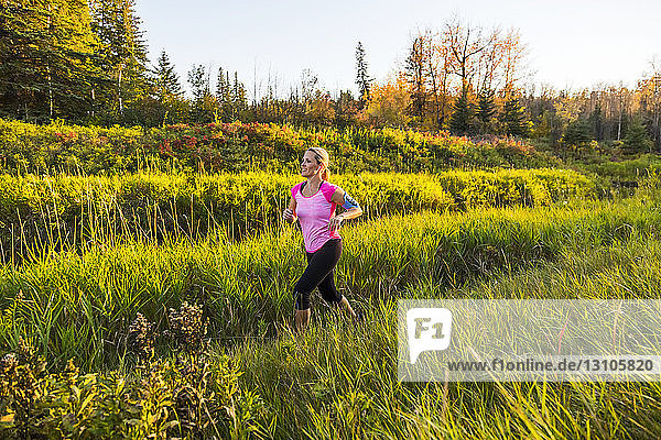 An attractive middle-aged woman wearing active wear and listening to music while running along a creek in a city park at sunset on a warm autumn evening; Edmonton  Alberta  Canada
