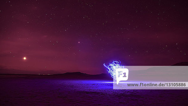 Bewegung von weißem Licht in einer Langzeitbelichtung mit einer dahinter stehenden Person und einem glühend roten Himmel in der Abenddämmerung  Great Salt Lake; Utah  Vereinigte Staaten von Amerika