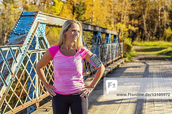 An attractive middle-aged woman pauses to rest on a bridge during a run on a beautiful warm fall evening in a city park; Edmonton Alberta Canada
