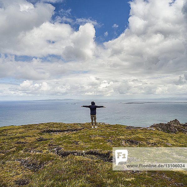 A woman stands with outstretched arms and looks out at the ocean and coastline while hiking at Brandon Point  Dingle Peninsula; Castlegregory  County Kerry  Ireland