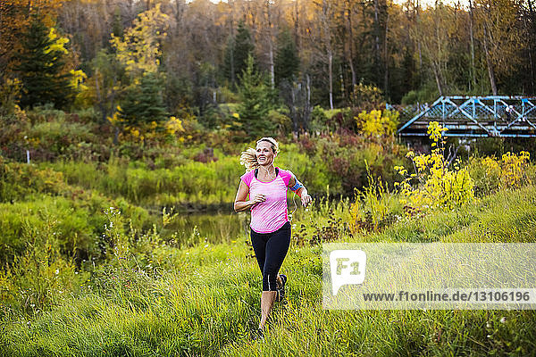 An attractive middle-aged woman wearing active wear and listening to music runs along a creek in a city park at sunset on a warm autumn evening; Edmonton  Alberta  Canada