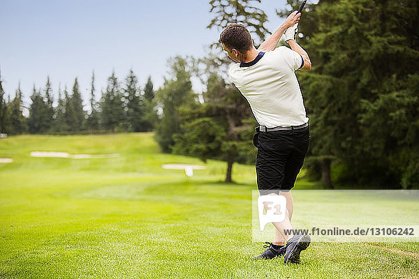 A male golfer driving a golf ball down the fairway of a golf course with the ball in mid-air; Edmonton  Alberta  Canada