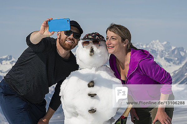 A couple enjoy the sights and scenery of Kluane National Park and Reserve on a bright sunny day while taking a self-portrait with a snowman; Haines Junction  Yukon  Canada