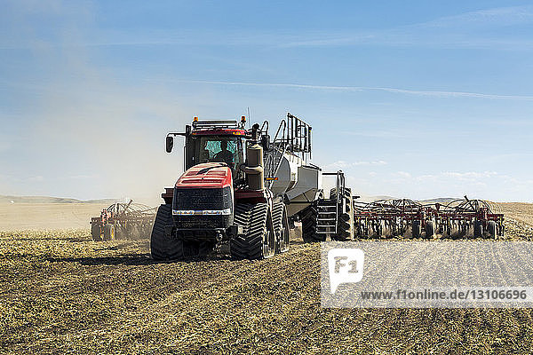 Traktor  der eine pneumatische Sämaschine zieht und ein Feld mit blauem Himmel und Wolken im Hintergrund sät; Rockyford  Alberta  Kanada