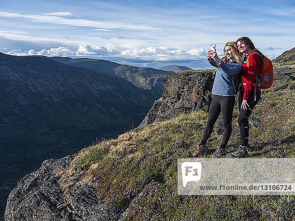 Two women using their cell phone to take a self-portrait and exploring the mountains and wilderness of the Yukon around Haines Junction; Yukon  Canada
