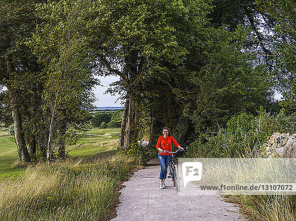 Eine Frau  die mit ihrem Fahrrad eine Straße beim Gleno Abbey Hotel und Golfplatz entlang fährt; County Galway  Irland
