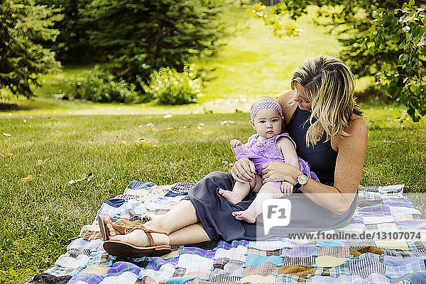 Eine Mutter und ihre kleine Tochter sitzen auf einer Picknickdecke und verbringen viel Zeit miteinander  während sie einen Familienausflug in einem Stadtpark an einem warmen Herbstnachmittag genießen; Edmonton  Alberta  Kanada
