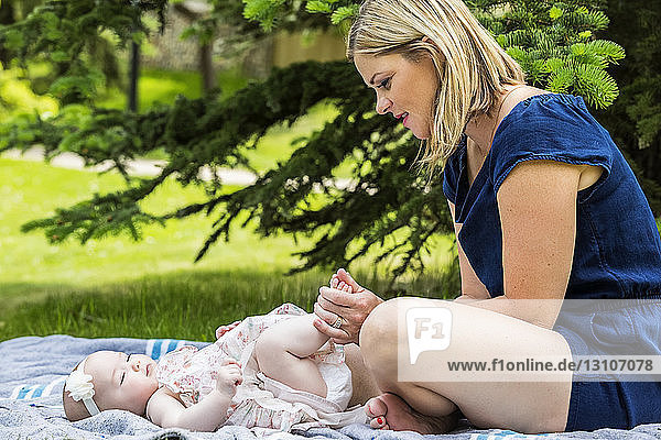 Eine junge Mutter spielt mit ihrem Baby auf einer Decke in einem Stadtpark an einem warmen Sommertag; Edmonton  Alberta  Kanada