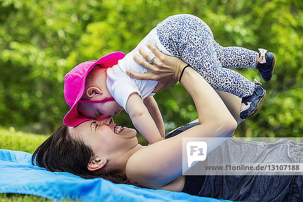 Eine junge Mutter verbringt viel Zeit mit ihrer kleinen Tochter und neckt sie  indem sie sie an einem warmen Sommertag in einem Park in die Luft hält; Edmonton  Alberta  Kanada