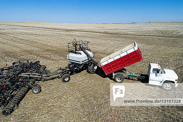 Aerial view of farmer filling an air seeder hopper with a truck in a field with blue sky in the background; Beiseker  Alberta  Canada