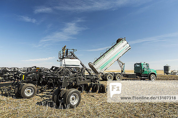 Landwirt steht auf einem Trichter  der mit einem Lastwagen gefüllt wird  auf einem Feld mit blauem Himmel und Wolken; Beiseker  Alberta  Kanada