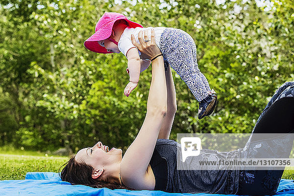 Eine junge Mutter verbringt viel Zeit mit ihrer kleinen Tochter und neckt sie  indem sie sie an einem warmen Sommertag in einem Park in die Luft hält; Edmonton  Alberta  Kanada