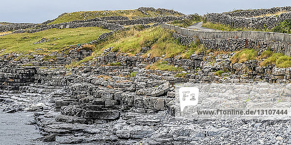 Steinmauern und eine Straße entlang der Küste von Inishmore  der größten der Aran-Inseln  Irland; Kilronan  Grafschaft Galway  Irland