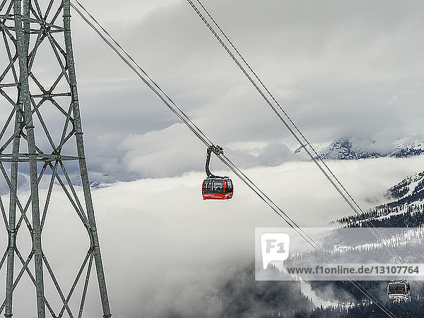 Red gondola lift on the cables above the mountains and clouds; Whistler British Columbia Canada