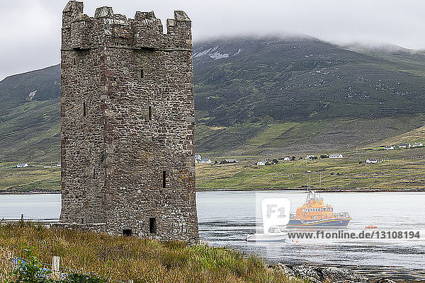 Ruinen eines Steinturms am Wasser mit vorbeifahrenden Booten; Achill Sound  County Mayo  Irland