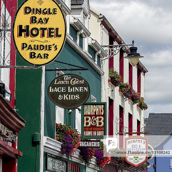 Aneinandergereihte Einzelhandelsschilder an Gebäuden in einer irischen Stadt; The Colony  County Kerry  Irland