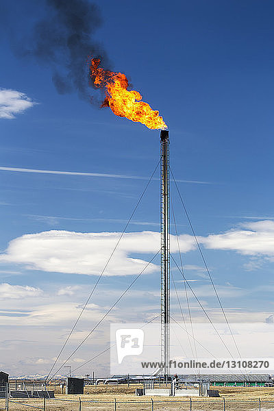 Tall gas plant flare with large fire flare and black smoke and blue sky and clouds in the background; Crossfield Alberta Canada