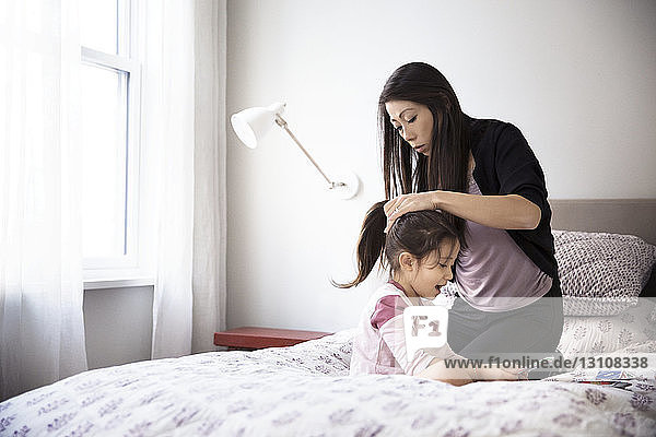 Mother tying hair of daughter on bed
