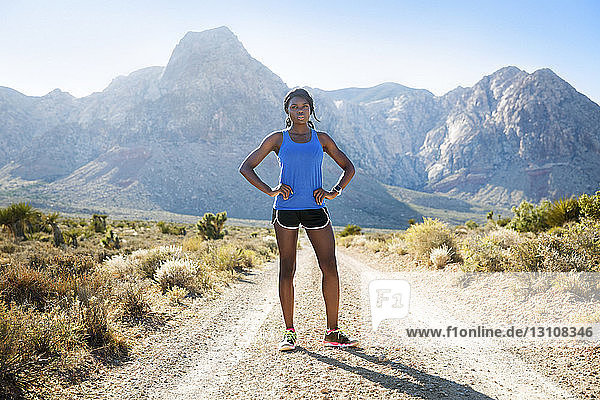 Confident female athlete standing on dirt road against mountains