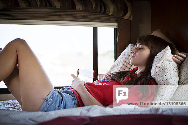 Frau benutzt Mobiltelefon  während sie im Wohnmobil auf dem Bett liegt
