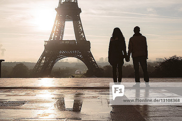 Silhouette couple looking at Eiffel Tower against sky during sunrise