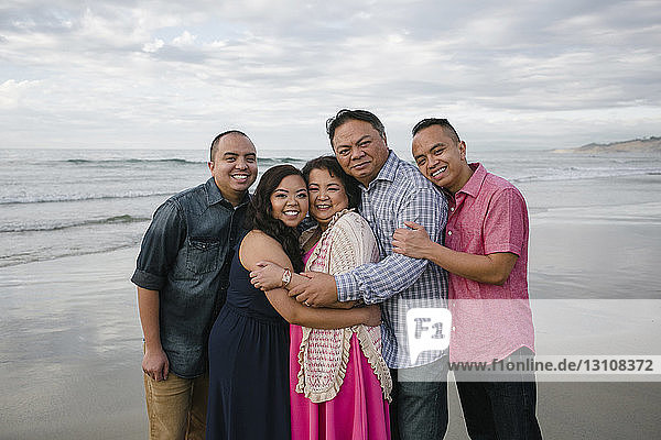 Portrait of happy family standing on shore at beach against sky