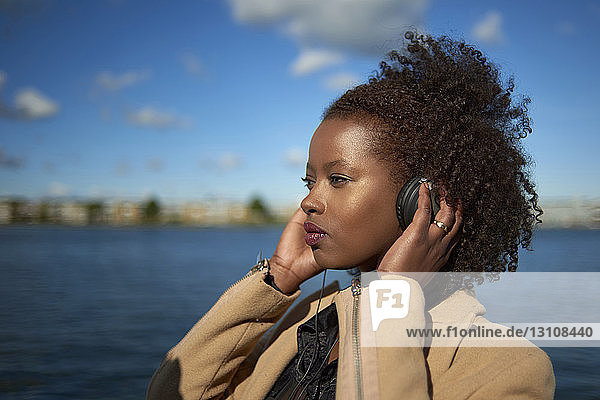 Frau schaut beim Musikhören weg  während sie am Fluss steht