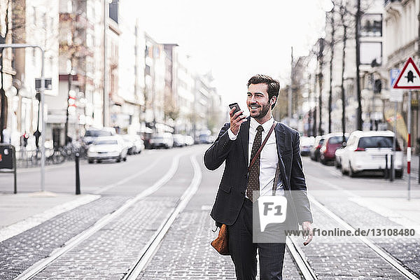 Businessman talking on mobile phone walking by railroad tracks in city