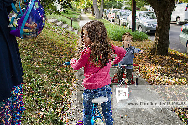 Mittelteil einer Mutter  die einen Helm hält  während Kinder im Herbst auf dem Fußweg Fahrrad fahren