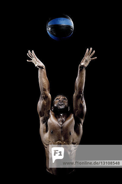 Muskulöser Mann wirft Ball in der Luft vor schwarzem Hintergrund