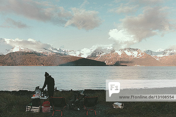 Schrägaufnahme einer Frau  die auf einem Campingplatz am See Essen zubereitet