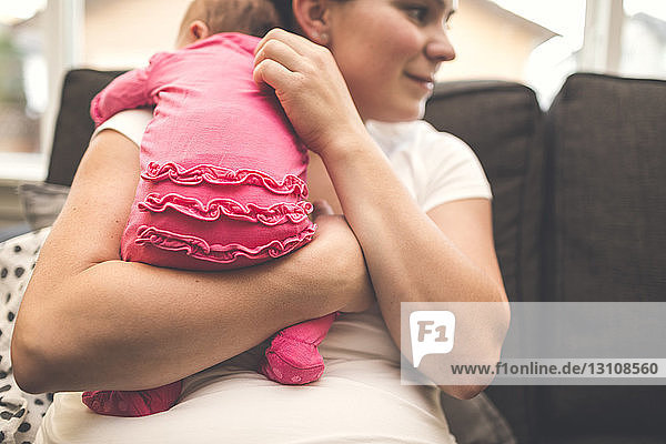 Mutter trägt neugeborene Tochter  während sie zu Hause auf dem Sofa sitzt